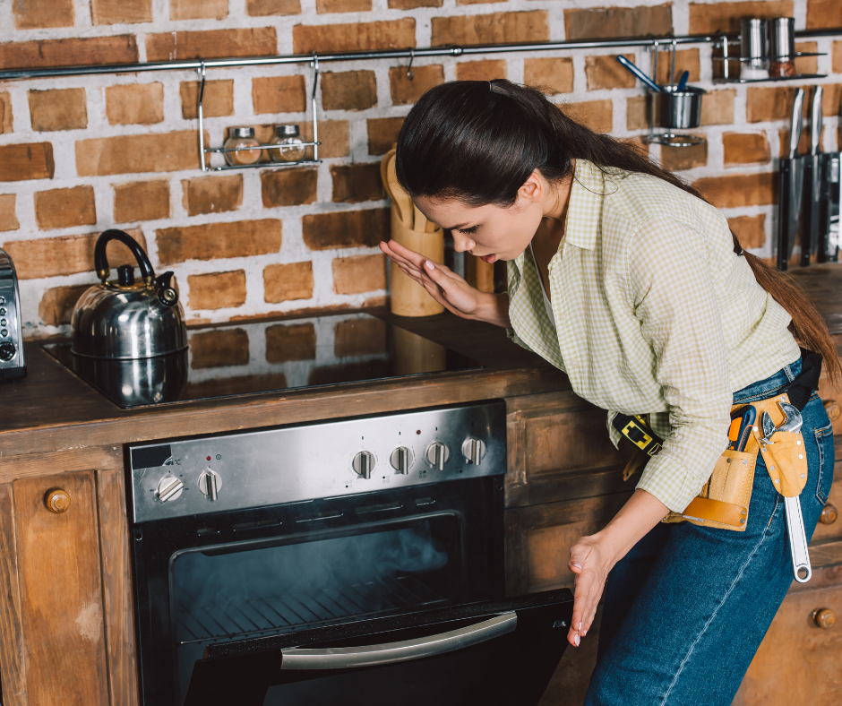 A woman inspecting a modern kitchen oven while wearing a tool belt, highlighting appliance shortages and repair challenges.